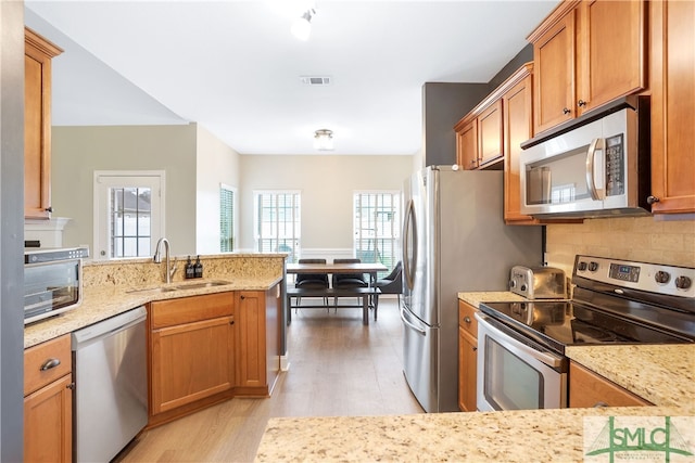 kitchen with sink, light hardwood / wood-style flooring, light stone counters, kitchen peninsula, and stainless steel appliances