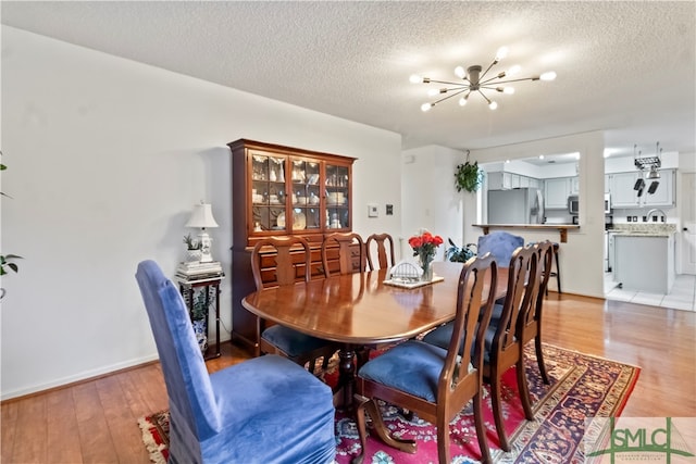 dining area with a textured ceiling, light hardwood / wood-style flooring, and a notable chandelier