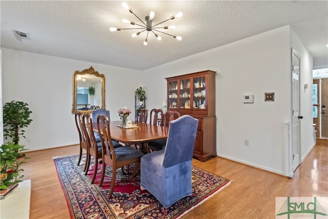 dining space with an inviting chandelier, a textured ceiling, and light hardwood / wood-style flooring