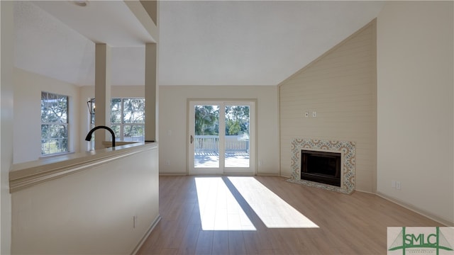 unfurnished living room featuring a tile fireplace, sink, high vaulted ceiling, and light wood-type flooring