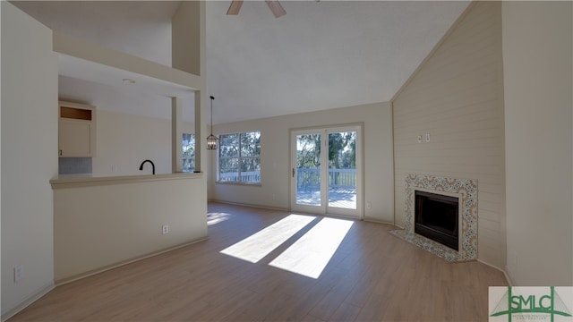 unfurnished living room with light wood-type flooring, ceiling fan, sink, high vaulted ceiling, and a fireplace