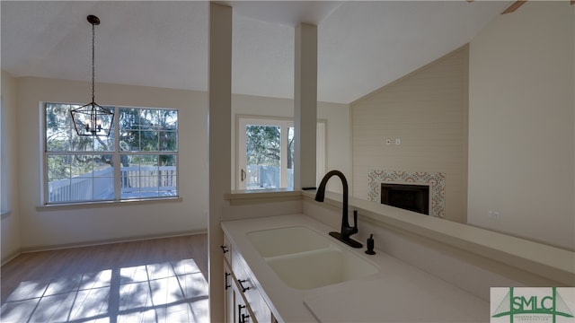 kitchen with a tile fireplace, sink, vaulted ceiling, decorative light fixtures, and a chandelier