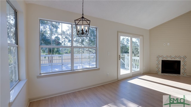 unfurnished living room featuring a textured ceiling, light hardwood / wood-style flooring, a notable chandelier, lofted ceiling, and a tiled fireplace