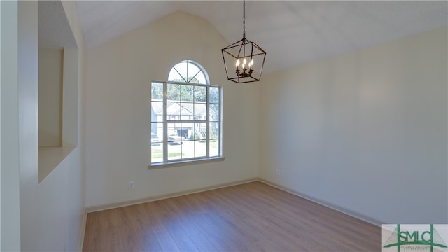 empty room featuring a chandelier, vaulted ceiling, and light wood-type flooring