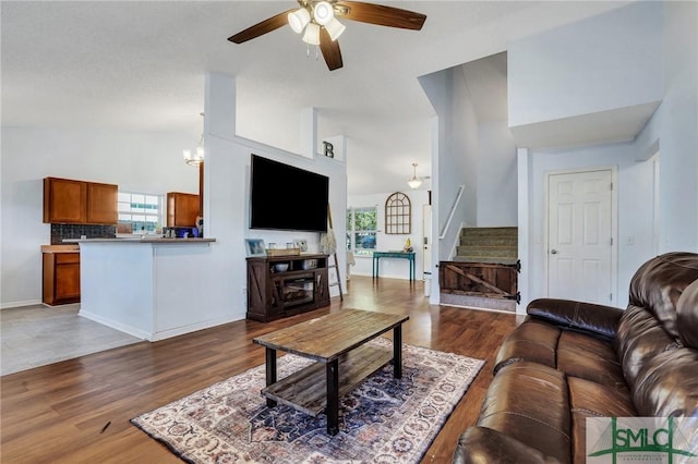 living room with ceiling fan with notable chandelier, hardwood / wood-style flooring, and high vaulted ceiling