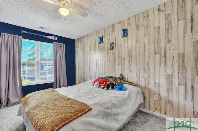 bedroom with a textured ceiling, ceiling fan, carpet, and wood walls