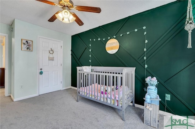 carpeted bedroom with a textured ceiling, ceiling fan, and a nursery area