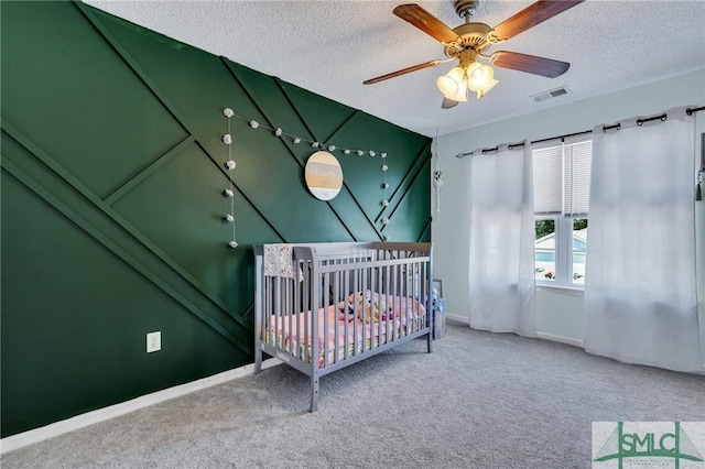 bedroom with a textured ceiling, ceiling fan, carpet, and a nursery area