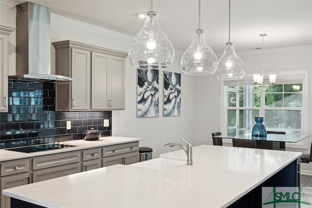 kitchen featuring black electric cooktop, gray cabinets, hanging light fixtures, and wall chimney range hood