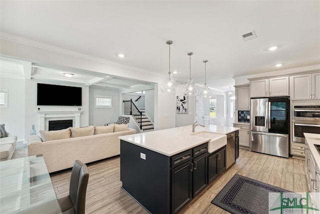 kitchen featuring decorative light fixtures, stainless steel appliances, a wealth of natural light, and an island with sink