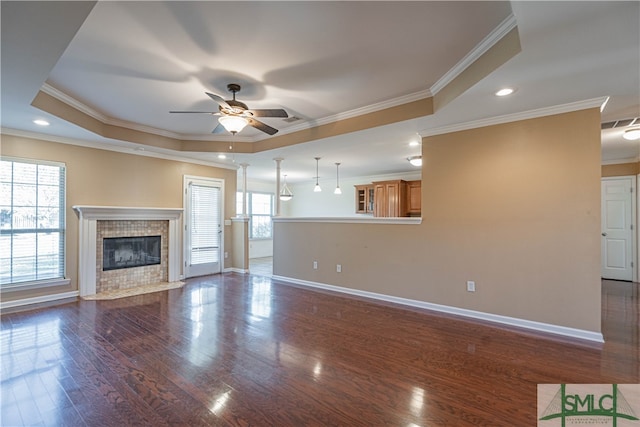 unfurnished living room featuring a tray ceiling, crown molding, ceiling fan, and dark wood-type flooring