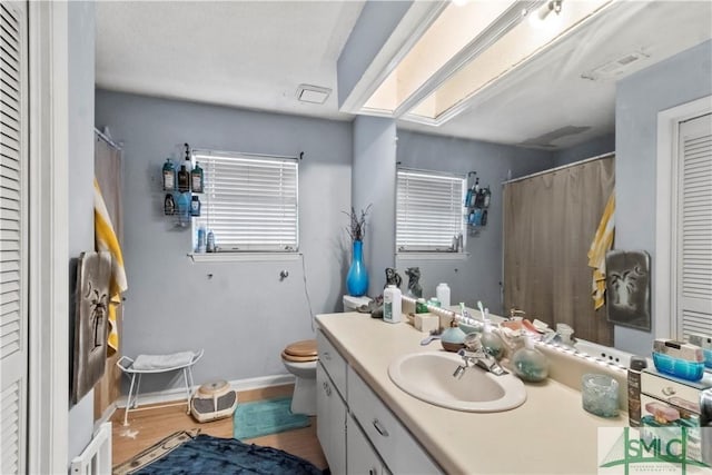 bathroom with a skylight, hardwood / wood-style flooring, vanity, and toilet