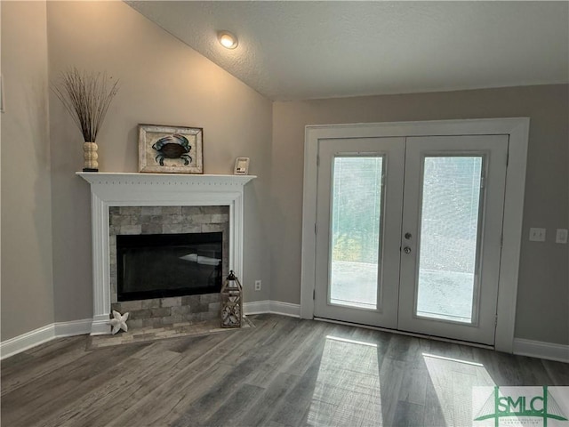 interior space with hardwood / wood-style floors, a stone fireplace, vaulted ceiling, and french doors