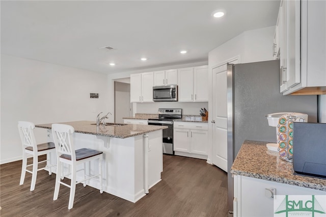 kitchen with white cabinetry, sink, dark wood-type flooring, stainless steel appliances, and a center island with sink