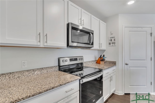 kitchen with appliances with stainless steel finishes, white cabinetry, dark wood-type flooring, and light stone counters