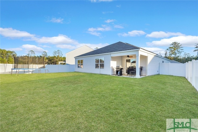 rear view of house with a lawn, ceiling fan, a trampoline, and a patio