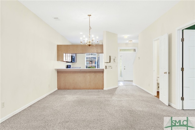 kitchen with light brown cabinets, carpet floors, an inviting chandelier, hanging light fixtures, and kitchen peninsula