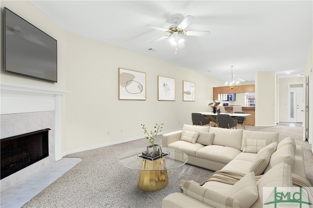 carpeted living room with a tiled fireplace and ceiling fan with notable chandelier