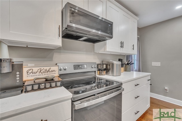 kitchen with appliances with stainless steel finishes, light hardwood / wood-style flooring, white cabinetry, and light stone counters