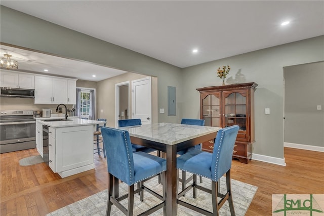 dining room featuring electric panel, light hardwood / wood-style flooring, and sink