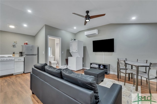 living room featuring ceiling fan, a wall mounted air conditioner, light hardwood / wood-style flooring, stacked washer / dryer, and vaulted ceiling