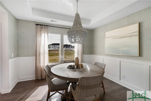 dining space with a tray ceiling, dark wood-style flooring, wainscoting, and visible vents