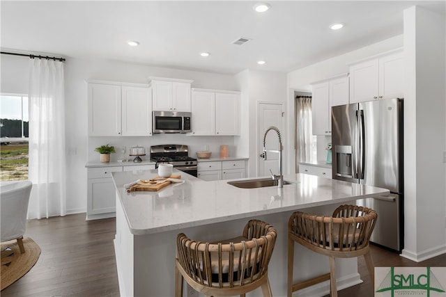 kitchen featuring visible vents, appliances with stainless steel finishes, white cabinets, a sink, and an island with sink