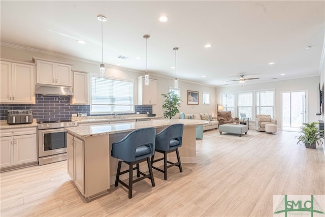 kitchen featuring a breakfast bar area, stainless steel electric range oven, decorative light fixtures, a center island, and light stone countertops