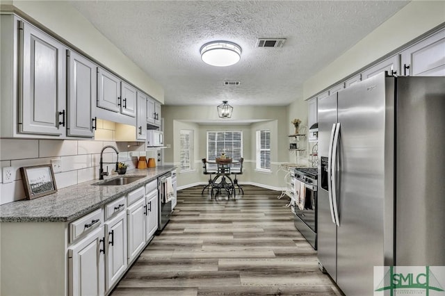 kitchen featuring sink, gray cabinets, tasteful backsplash, light stone counters, and stainless steel appliances