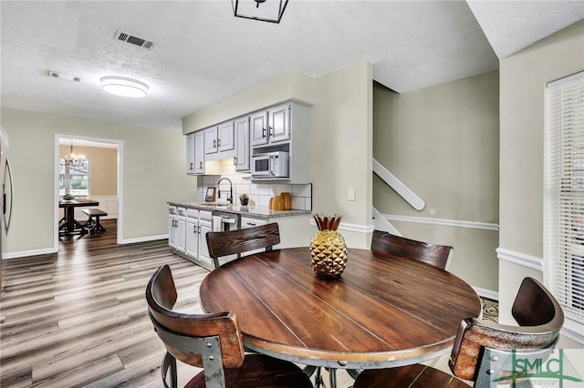 dining area with a textured ceiling, light hardwood / wood-style flooring, a notable chandelier, and sink