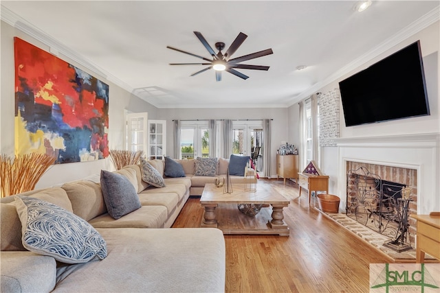 living room featuring light wood-type flooring, a brick fireplace, ceiling fan, and ornamental molding