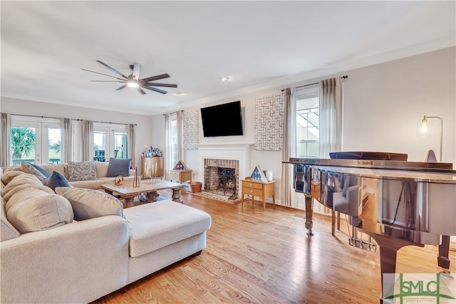 living room featuring a brick fireplace, ceiling fan, ornamental molding, and light hardwood / wood-style flooring