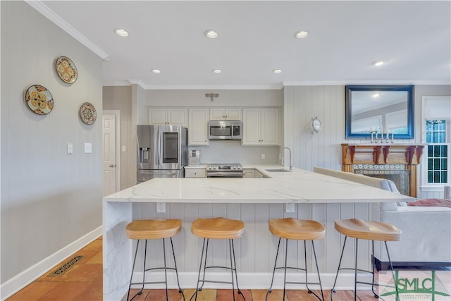 kitchen featuring a kitchen bar, appliances with stainless steel finishes, light stone counters, ornamental molding, and sink