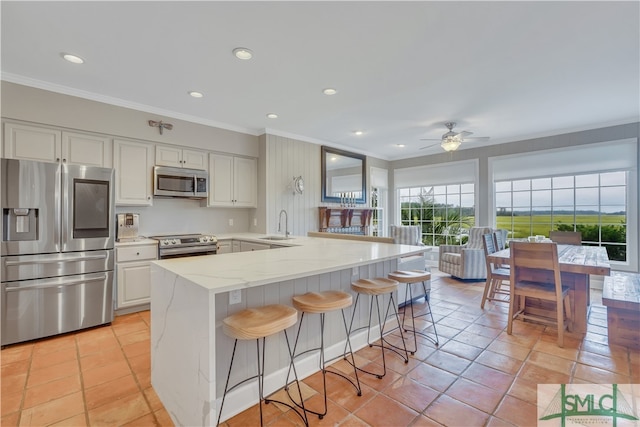 kitchen featuring a kitchen bar, appliances with stainless steel finishes, light stone counters, ceiling fan, and white cabinetry