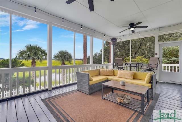 sunroom with ceiling fan and a water view