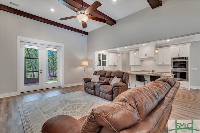 living room with french doors, light wood-type flooring, ceiling fan, and beam ceiling