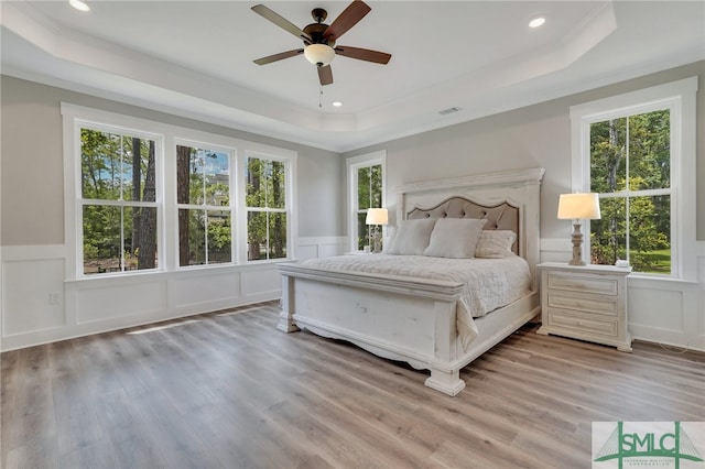 unfurnished bedroom featuring hardwood / wood-style floors, a tray ceiling, multiple windows, and ceiling fan