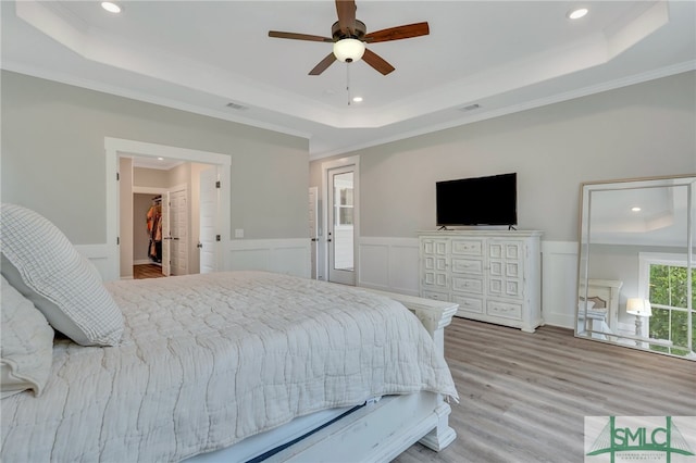 bedroom with ceiling fan, a spacious closet, a raised ceiling, crown molding, and light hardwood / wood-style floors