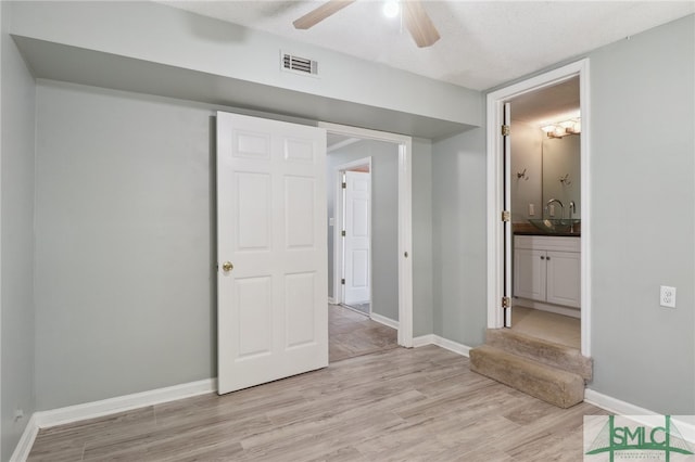 unfurnished bedroom featuring ceiling fan, light wood-type flooring, a textured ceiling, and ensuite bath