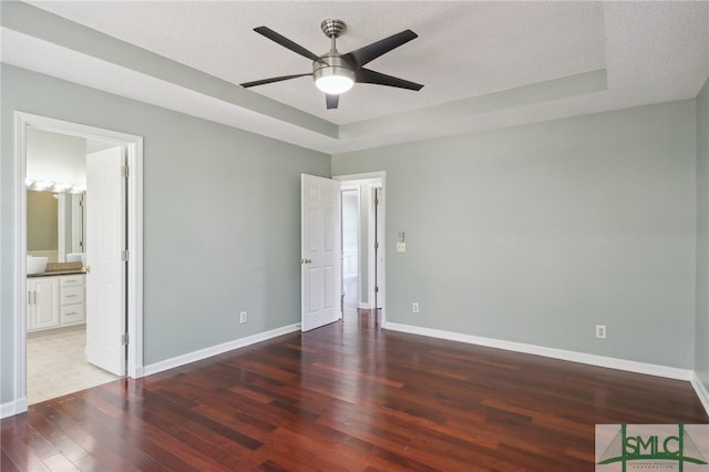 unfurnished bedroom featuring ceiling fan, ensuite bathroom, dark wood-type flooring, and a textured ceiling