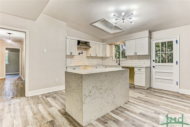 kitchen with wall chimney exhaust hood, a kitchen island, tasteful backsplash, white cabinets, and light wood-type flooring