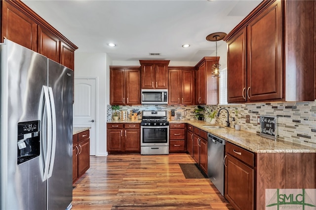 kitchen featuring pendant lighting, backsplash, sink, light wood-type flooring, and appliances with stainless steel finishes