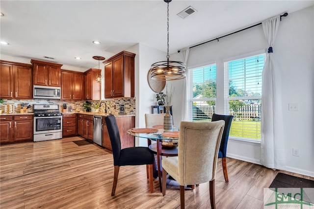 kitchen with appliances with stainless steel finishes, tasteful backsplash, sink, pendant lighting, and light hardwood / wood-style floors