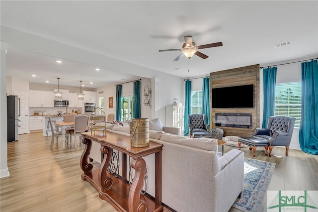 living room with ceiling fan, a large fireplace, and light wood-type flooring