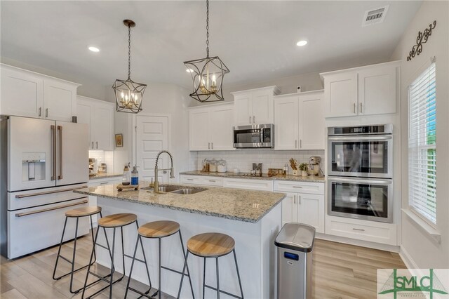 kitchen with appliances with stainless steel finishes, light wood-type flooring, sink, a center island with sink, and white cabinetry