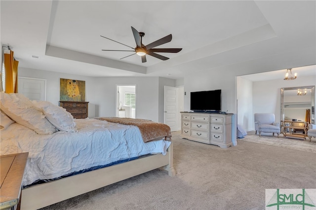 bedroom with ceiling fan with notable chandelier, a tray ceiling, and light colored carpet