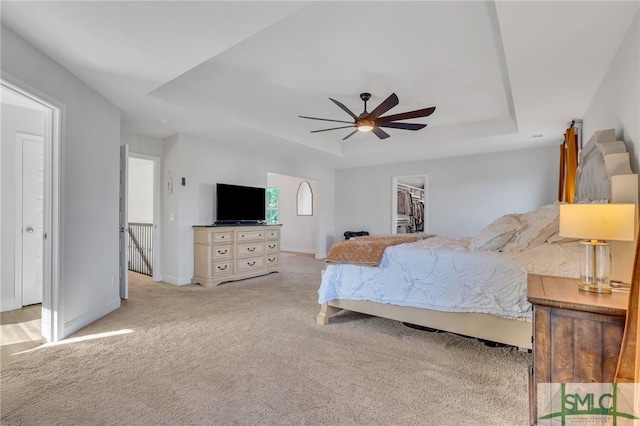 bedroom with light carpet, a tray ceiling, ceiling fan, a spacious closet, and a closet