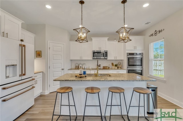 kitchen with stainless steel appliances, a kitchen island with sink, decorative light fixtures, a notable chandelier, and white cabinets