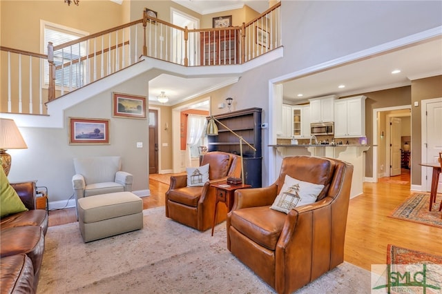 living room featuring crown molding, a high ceiling, and light hardwood / wood-style flooring