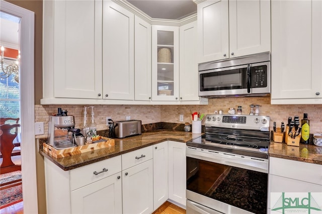 kitchen featuring backsplash, dark stone counters, ornamental molding, white cabinetry, and stainless steel appliances